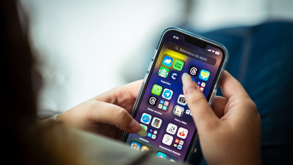 Mulher segura um smartphone que exibe diversos aplicativos na tela.