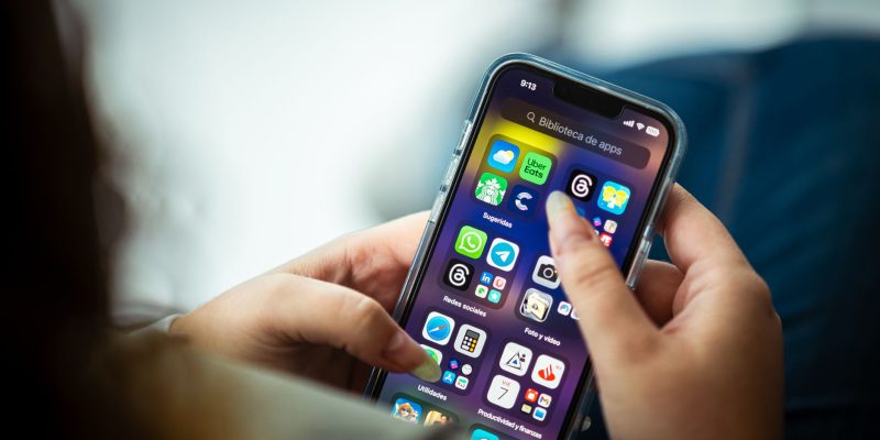 Mulher segura um smartphone que exibe diversos aplicativos na tela.