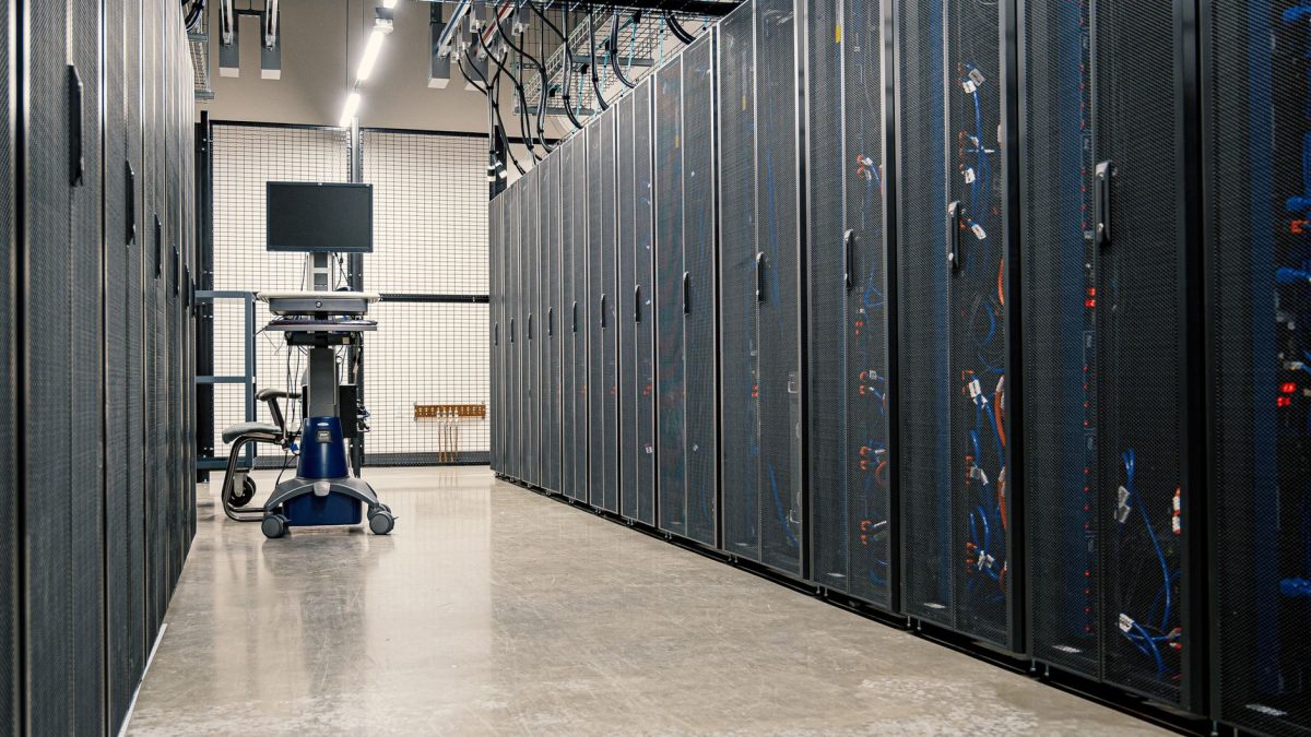 Fileiras de gabinetes metálicos com servidores, equipamentos de rede e cabos em um data center moderno