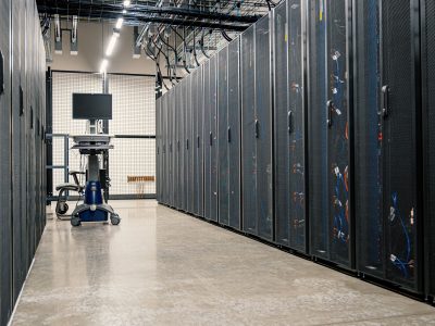 Fileiras de gabinetes metálicos com servidores, equipamentos de rede e cabos em um data center moderno