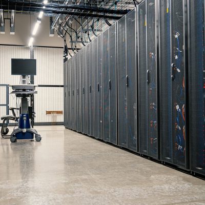 Fileiras de gabinetes metálicos com servidores, equipamentos de rede e cabos em um data center moderno