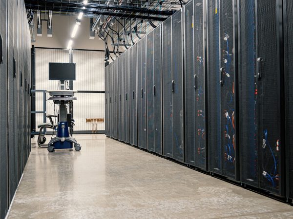 Fileiras de gabinetes metálicos com servidores, equipamentos de rede e cabos em um data center moderno
