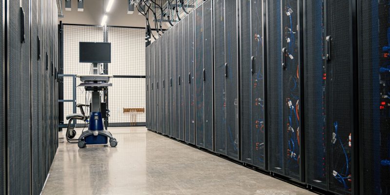 Fileiras de gabinetes metálicos com servidores, equipamentos de rede e cabos em um data center moderno