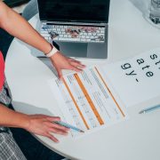 Pessoa analisando documentos e um laptop sobre uma mesa, em uma atividade de planejamento e avaliação de projetos.