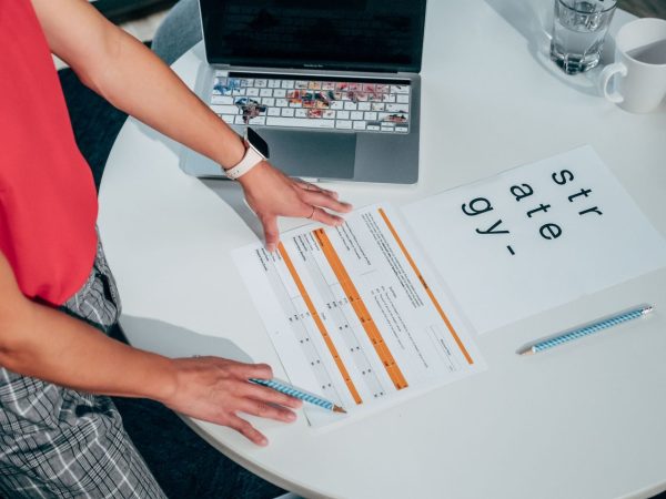 Pessoa analisando documentos e um laptop sobre uma mesa, em uma atividade de planejamento e avaliação de projetos.