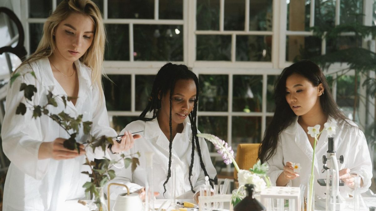 Três mulheres cientistas examinam plantas em um laboratório.