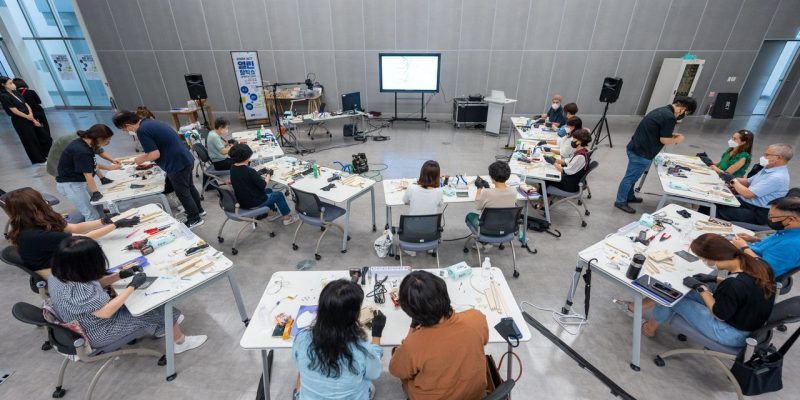 Estudantes participam de uma atividade prática com equipamentos tecnológicos em uma sala de aula.