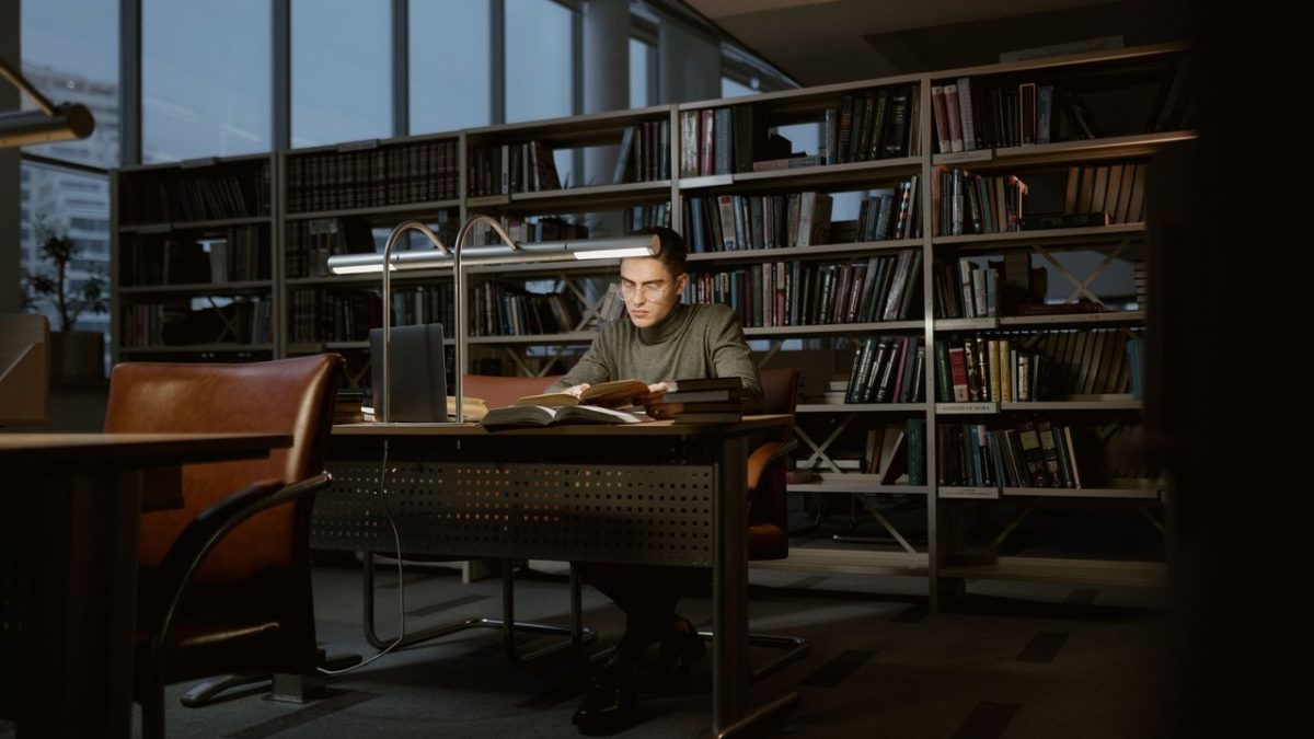 Pesquisador estuda concentrado em uma biblioteca cercado por livros.