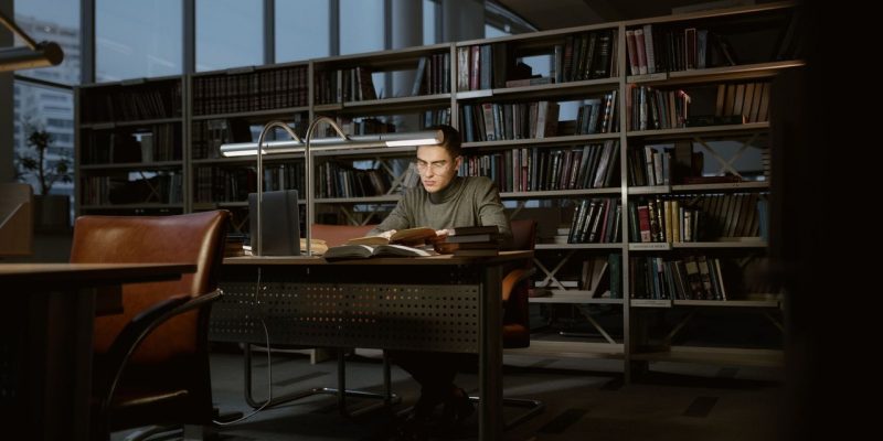 Pesquisador estuda concentrado em uma biblioteca cercado por livros.