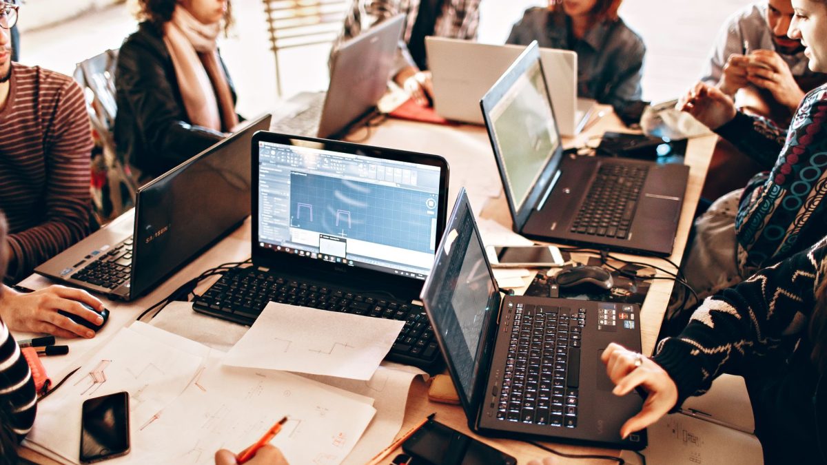 Grupo diverso de profissionais trabalha em conjunto com laptops e papéis em um escritório moderno.