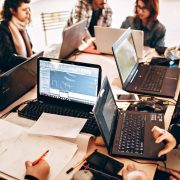 Grupo diverso de profissionais trabalha em conjunto com laptops e papéis em um escritório moderno.
