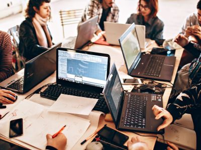 Grupo diverso de profissionais trabalha em conjunto com laptops e papéis em um escritório moderno.