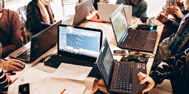 Grupo diverso de profissionais trabalha em conjunto com laptops e papéis em um escritório moderno.
