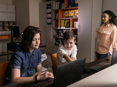 Estudantes usam laptops em sala de aula enquanto um professor acompanha a atividade.