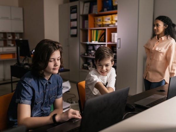 Estudantes usam laptops em sala de aula enquanto um professor acompanha a atividade.