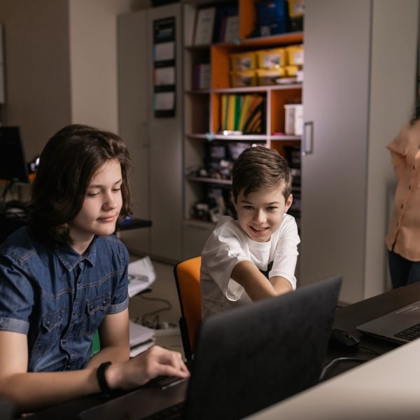 Estudantes usam laptops em sala de aula enquanto um professor acompanha a atividade.